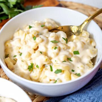 A bowl of creamy white cheddar mac and cheese topped with chopped parsley.
