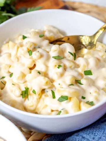 A bowl of creamy white cheddar mac and cheese topped with chopped parsley.