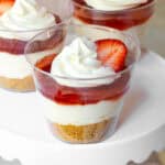 Strawberry cheesecake cups with graham cracker crust, cream filling, strawberry jam, and whipped topping with a strawberry slice.