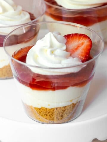Strawberry cheesecake cups with graham cracker crust, cream filling, strawberry jam, and whipped topping with a strawberry slice.