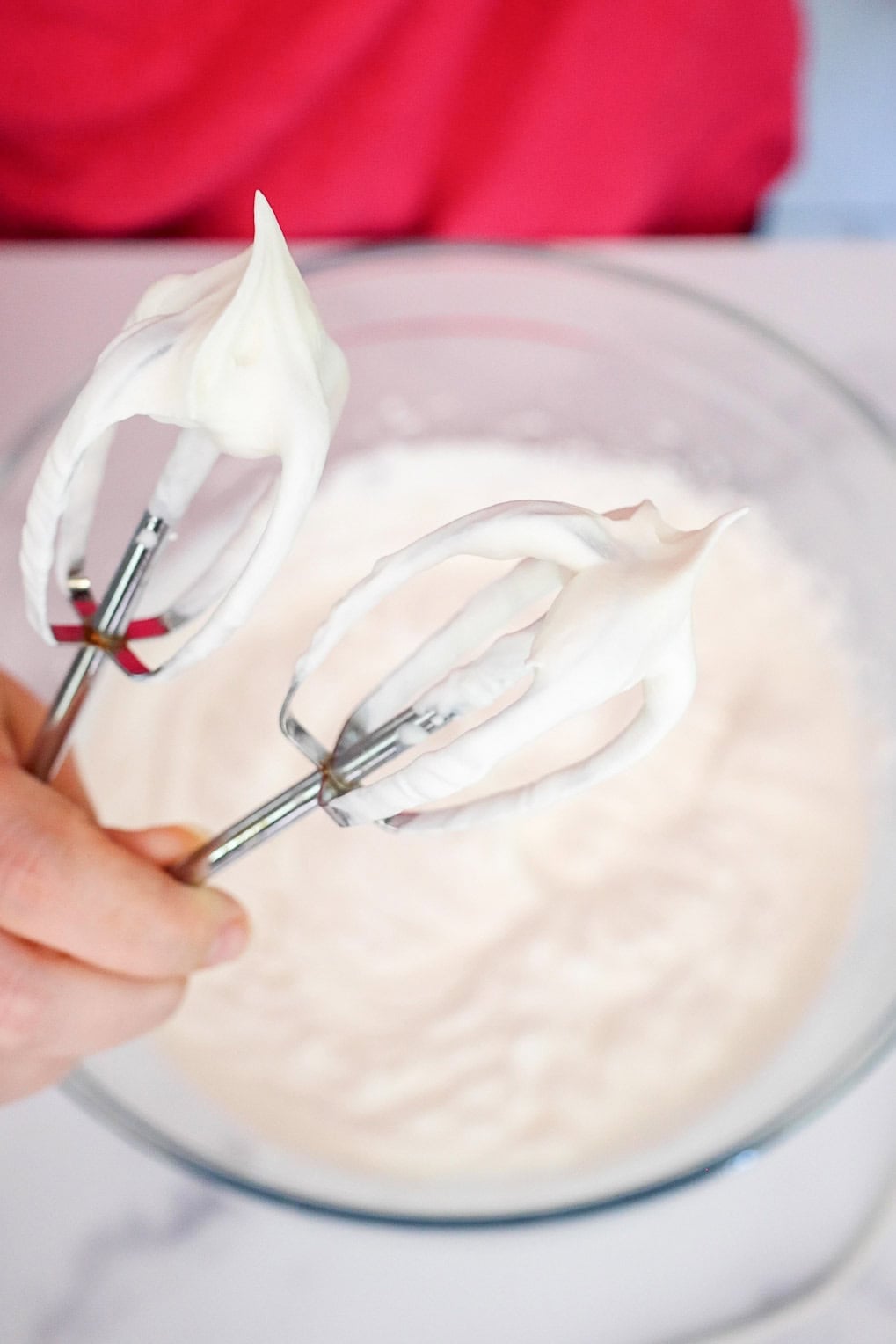 Electric beaters with stiff whipped cream peaks above a glass bowl.