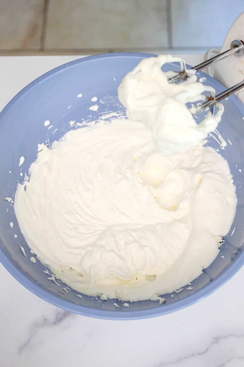 Whipped cheesecake filling in a large mixing bowl with electric beaters resting inside.
