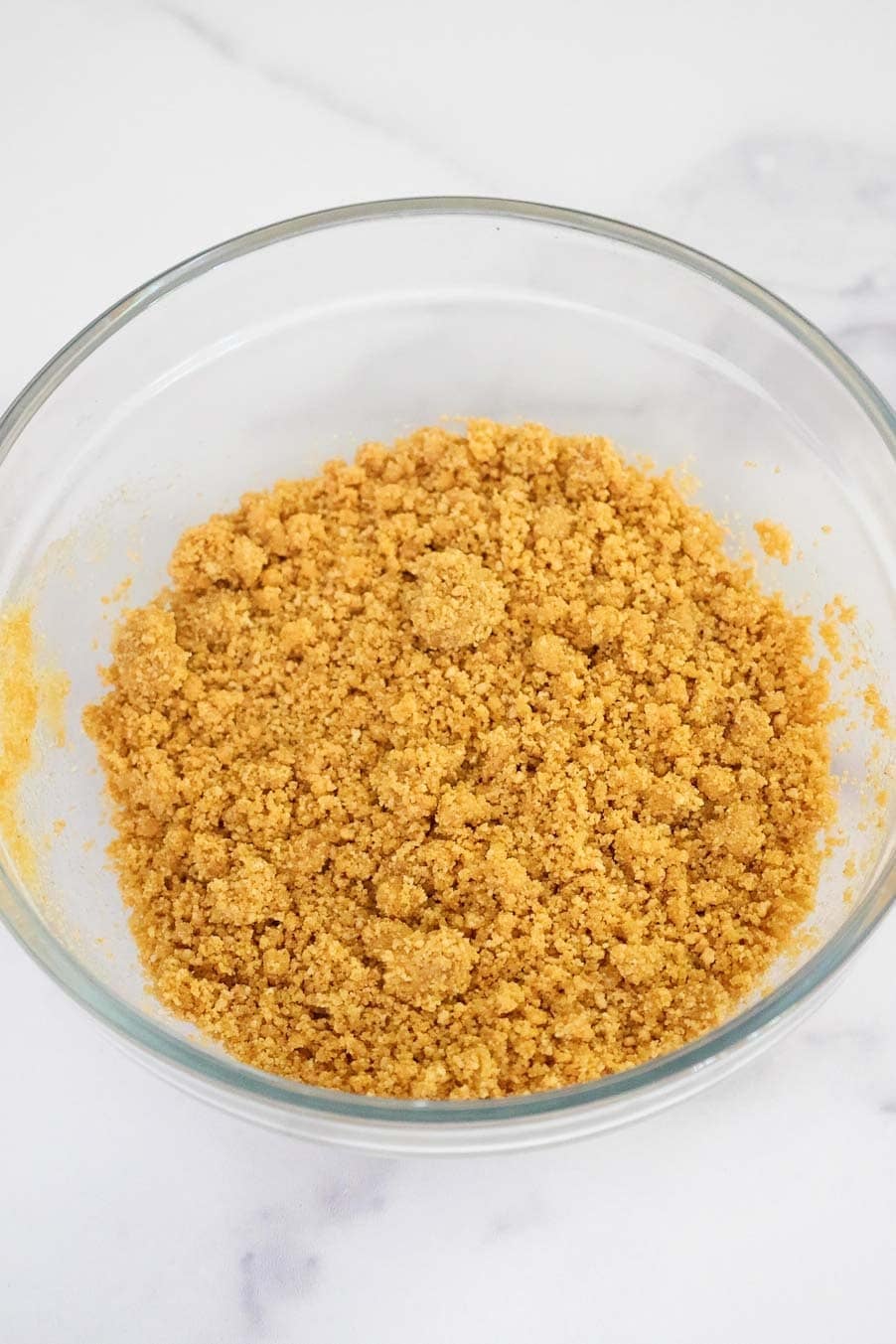 Thick crumble of crushed graham cracker and butter mixture in a glass bowl.