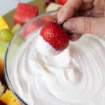 A hand holding a fresh strawberry dipped in fluffy marshmallow fruit dip.