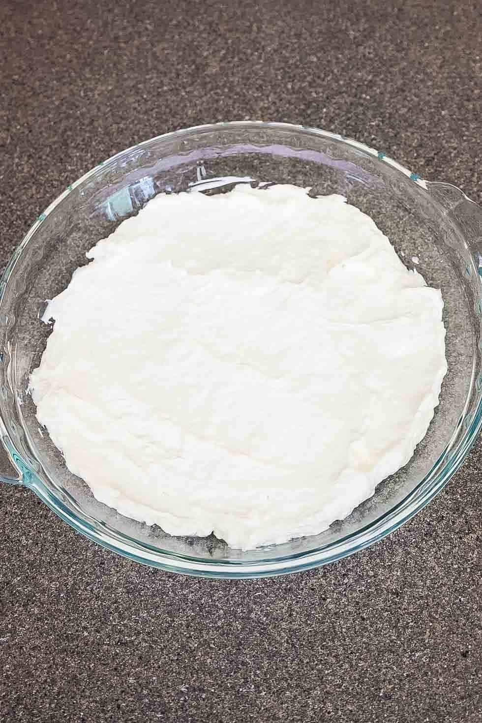 A glass baking dish with the creamy white base layer of the dip spread evenly across the bottom.