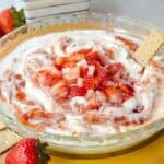 Strawberry cheesecake dip topped with swirled strawberry jam and diced fresh strawberries served in a glass pie dish.