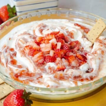 Strawberry cheesecake dip topped with swirled strawberry jam and diced fresh strawberries served in a glass pie dish.