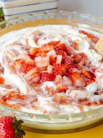 Strawberry cheesecake dip topped with swirled strawberry jam and diced fresh strawberries served in a glass pie dish.