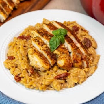 Plate of marry me chicken orzo with sun-dried tomatoes and sliced chicken breast.