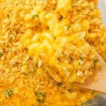 A wooden spoon scooping old fashioned baked mac and cheese topped with Ritz crackers from a baking dish.