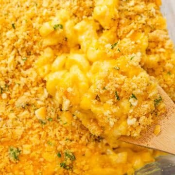A wooden spoon scooping old fashioned baked mac and cheese topped with Ritz crackers from a baking dish.