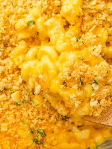 A wooden spoon scooping old fashioned baked mac and cheese topped with Ritz crackers from a baking dish.