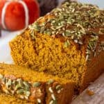 Sliced pumpkin bread showing its fluffy interior and pepita crusted top, set against a fall-themed background.