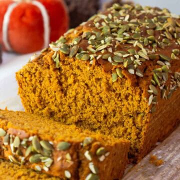 Sliced pumpkin bread showing its fluffy interior and pepita crusted top, set against a fall-themed background.