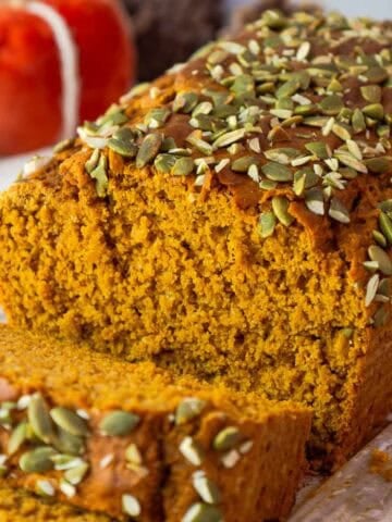 Sliced pumpkin bread showing its fluffy interior and pepita crusted top, set against a fall-themed background.