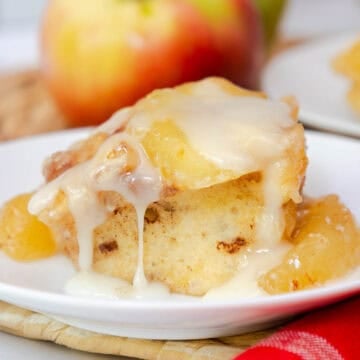 A cinnamon roll on a plate topped with apple pie filling and dripping with icing.