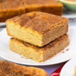 Two thick, golden-brown snickerdoodle cookie bars stacked on a plate, topped with a crackly cinnamon-sugar crust.