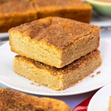 Two thick, golden-brown snickerdoodle cookie bars stacked on a plate, topped with a crackly cinnamon-sugar crust.