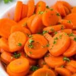 Brown sugar and honey glazed canned carrots, glistening in their syrup and sprinkled with fresh parsley.