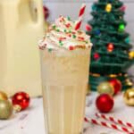 Tall glass of eggnog dirty soda topped with whipped cream, red and green holiday sprinkles, and a dusting of cinnamon, served with a red-striped straw.