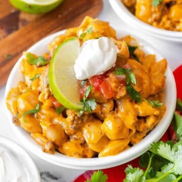 Small white bowl filled with taco mac and cheese, garnished with sour cream, salsa, chopped cilantro, and a lime slice.