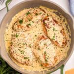 Skillet with four creamy garlic chicken breasts coated in sauce and topped with chopped fresh parsley.