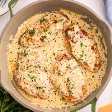 Skillet with four creamy garlic chicken breasts coated in sauce and topped with chopped fresh parsley.