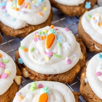 Close up of carrot cake mix cookies with thick cream cheese frosting, colorful sprinkles, and carrot shaped candy decorations on top.