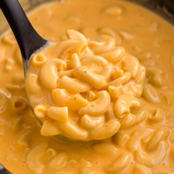 Close up of a spoonful of crockpot Velveeta mac and cheese with tender elbow macaroni covered in thick melted cheese sauce. The glossy texture shows how rich and creamy the dish is.