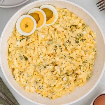 Close up of dill pickle egg salad in a serving bowl topped with sliced hard boiled eggs and sprinkled with fresh dill.