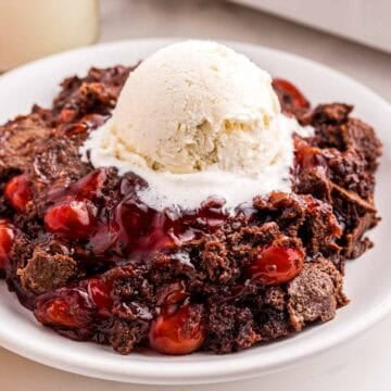 Cherry dump cake on a plate with a scoop of vanilla ice cream on top.