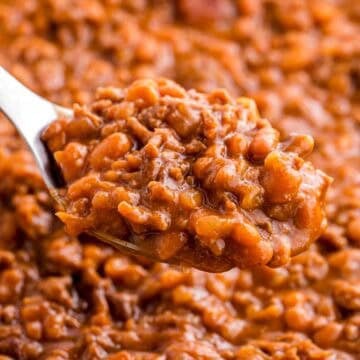 Spoonful of baked beans with ground beef held above the dish to show the thick texture and rich sauce. Tender beans and crumbled beef are visible in the close up.