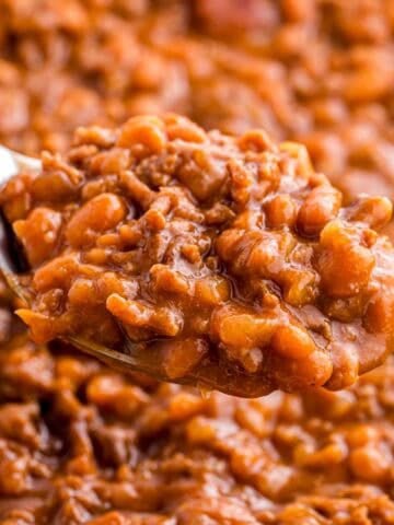 Spoonful of baked beans with ground beef held above the dish to show the thick texture and rich sauce. Tender beans and crumbled beef are visible in the close up.