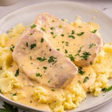 Crockpot ranch pork chops are served over mashed potatoes with creamy sauce spooned around them. Chopped parsley is sprinkled over the pork and potatoes.