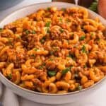 A bowl filled with American goulash with elbow macaroni ground beef and tomato sauce and topped with chopped parsley.
