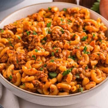 A bowl filled with American goulash with elbow macaroni ground beef and tomato sauce and topped with chopped parsley.