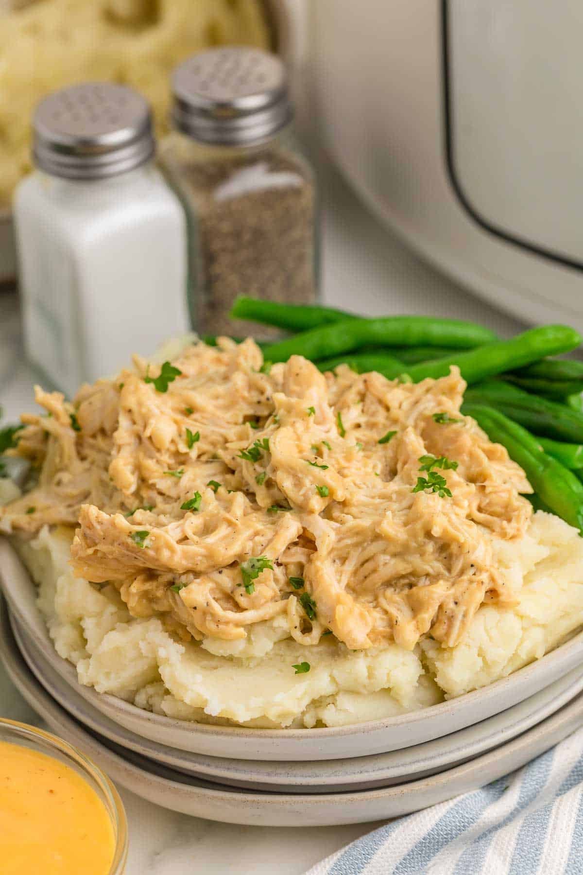 Shredded honey mustard chicken served over mashed potatoes with green beans on the side. Chopped parsley adds a fresh garnish.