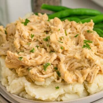 Shredded honey mustard chicken served over mashed potatoes with green beans on the side. Chopped parsley adds a fresh garnish.