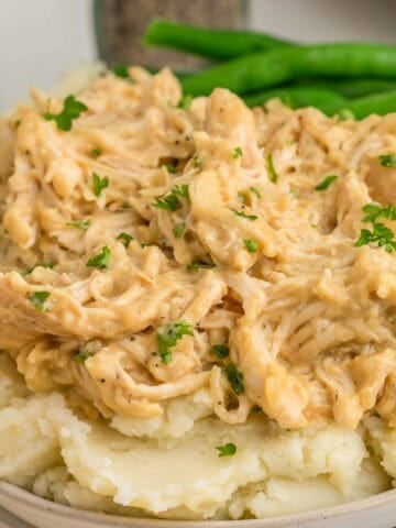 Shredded honey mustard chicken served over mashed potatoes with green beans on the side. Chopped parsley adds a fresh garnish.