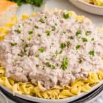 Finished ground beef stroganoff served over wide egg noodles and garnished with chopped parsley. The creamy beef sauce is spooned generously across the noodles.