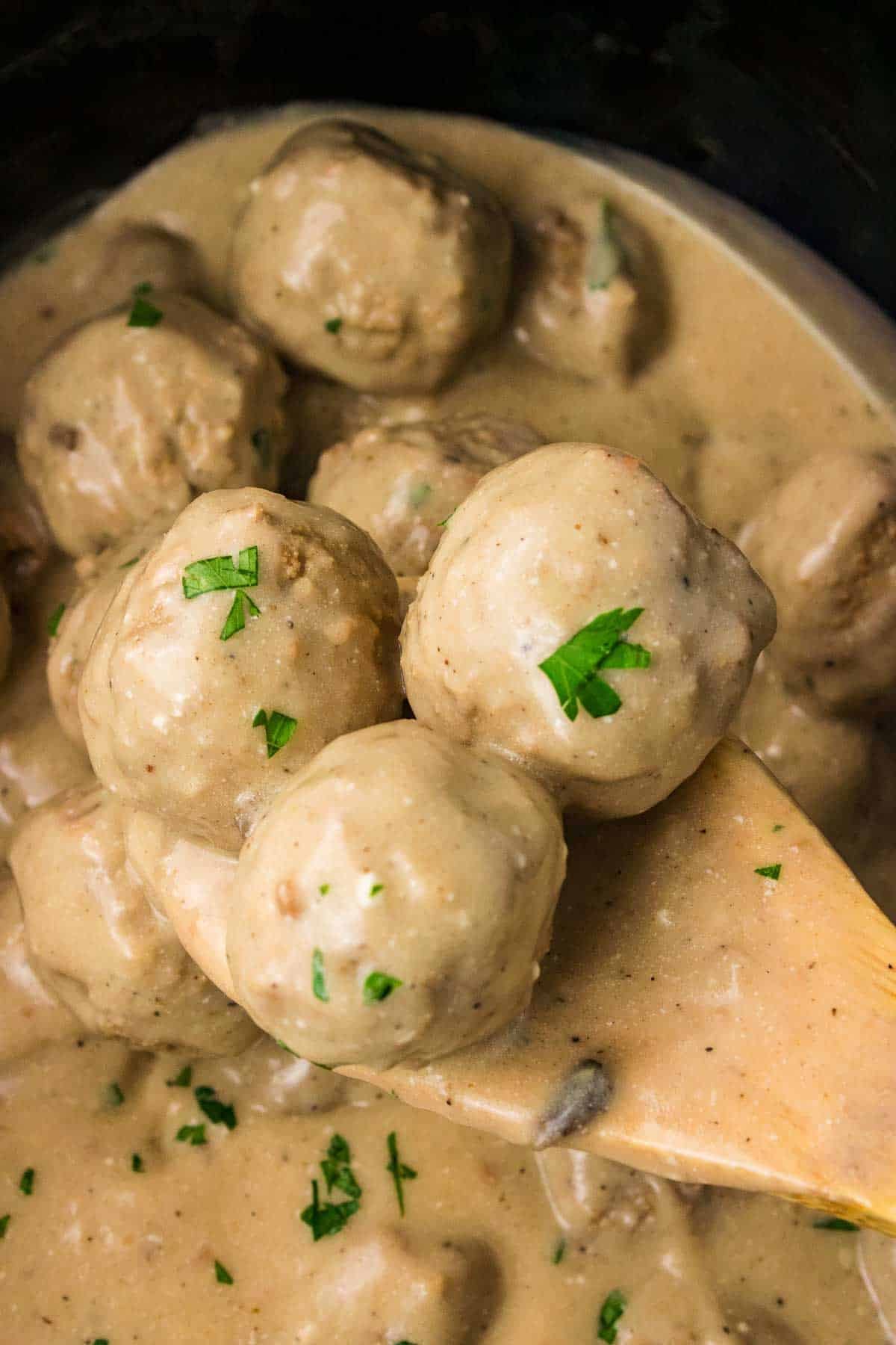 Crockpot Swedish meatballs coated in thick creamy mushroom sauce and sprinkled with chopped parsley. A serving spoon lifts several meatballs from the finished sauce.