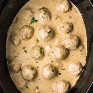 Close view of finished Crockpot Swedish meatballs coated in creamy mushroom sauce inside the slow cooker. Chopped parsley is scattered over the sauce and meatballs.