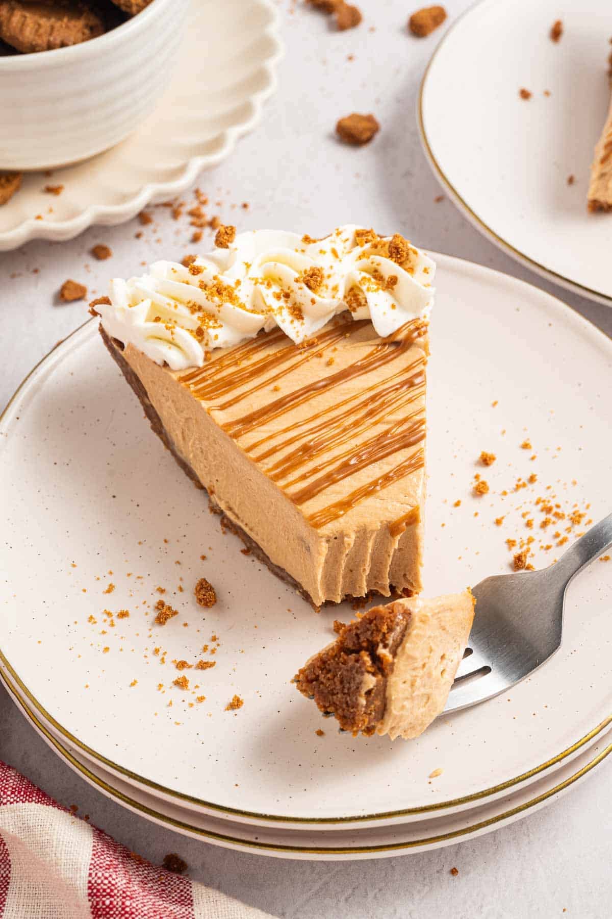 Slice of no bake Biscoff cookie butter pie with a thick creamy filling and crumb crust. The slice is topped with whipped cream. Crushed Biscoff cookies and a cookie butter drizzle finish the pie.