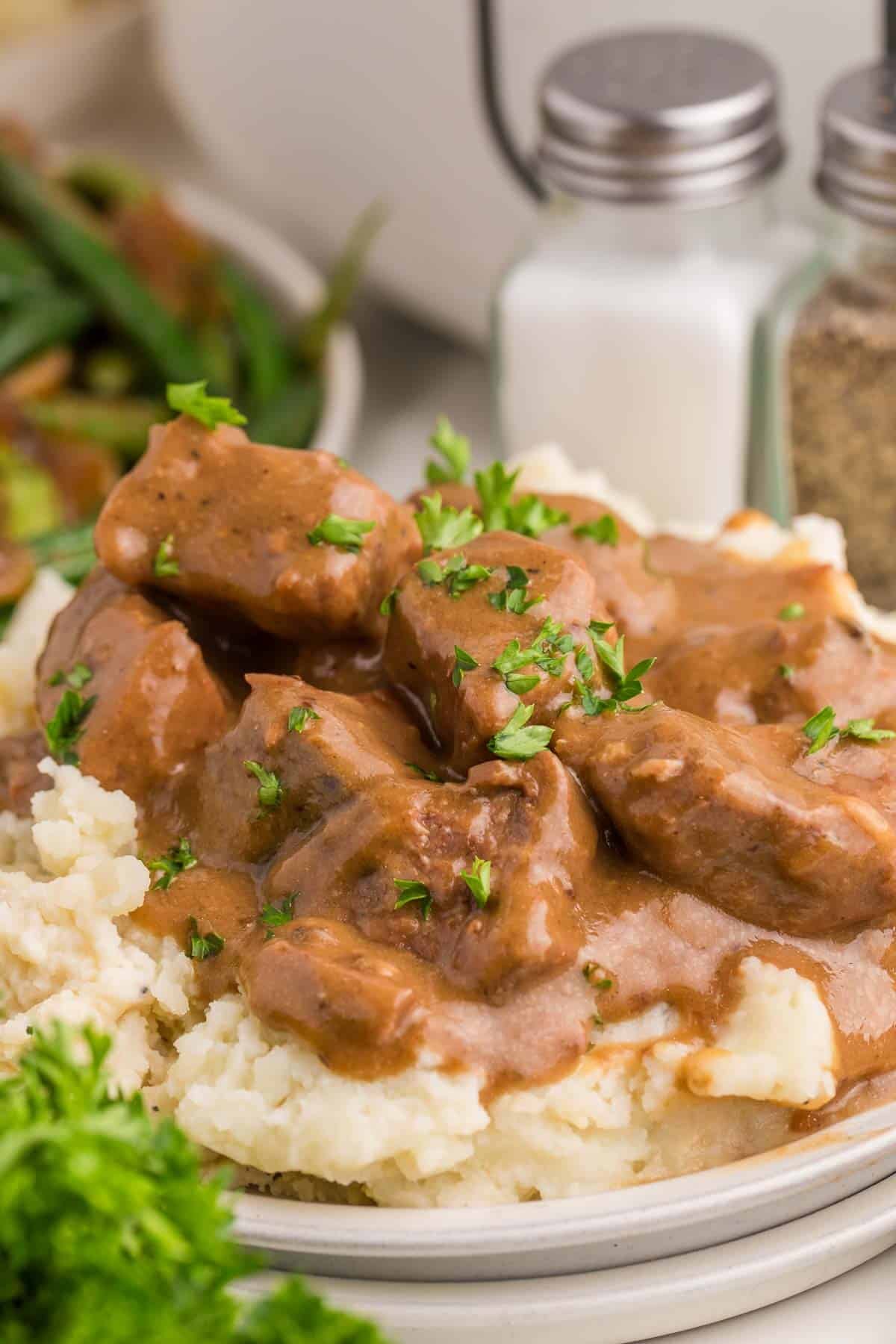 Slow cooker beef tips coated in thick brown gravy and spooned over mashed potatoes. Chopped parsley adds a fresh garnish to the finished dish.