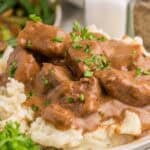 Close view of tender slow cooker beef tips covered in rich brown gravy and served over mashed potatoes. Chopped parsley is sprinkled over the beef before serving.