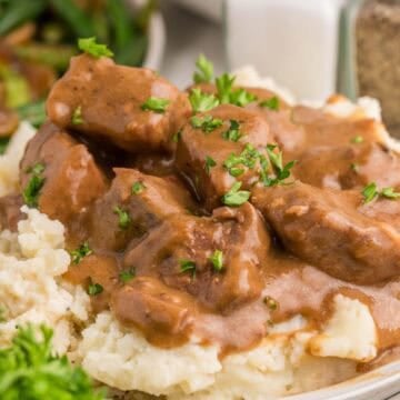 Close view of tender slow cooker beef tips covered in rich brown gravy and served over mashed potatoes. Chopped parsley is sprinkled over the beef before serving.
