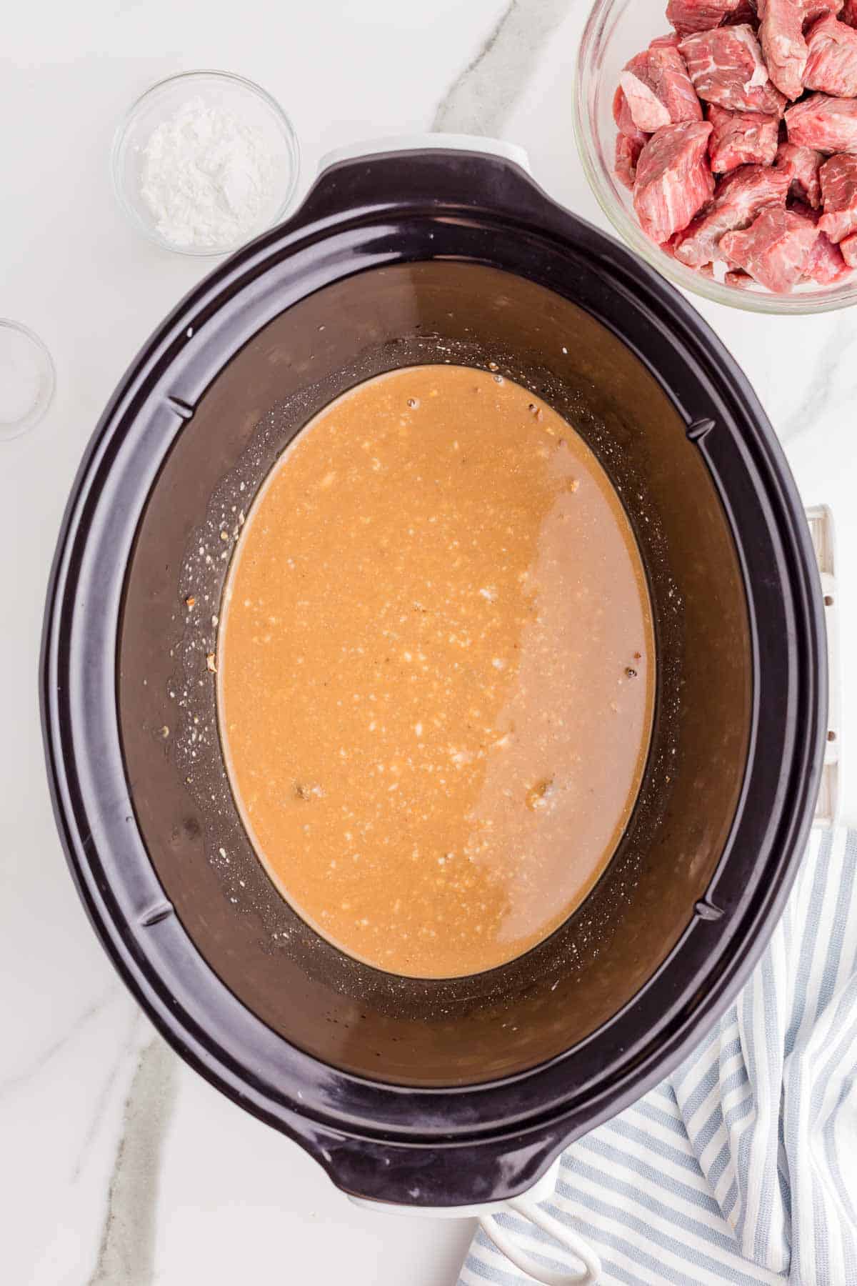 Beef broth. Cream of mushroom soup. Onion soup mix. And brown gravy mix combined in the slow cooker to form the gravy base. The seasoned raw beef is ready to be added.