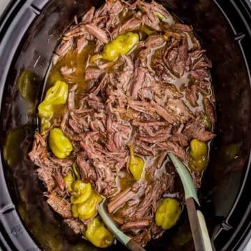 Tender shredded Mississippi pot roast with whole pepperoncini peppers in a slow cooker.